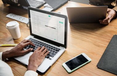 Person typing on laptop with phone and coffee